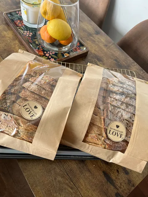Deux miches tranchées dans des sacs kraft à fenêtre, chacun avec un autocollant rond « Handmade with love ».
