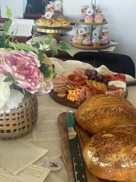 Une table dressée pour des invités : une planche à partager, des petits gâteaux, des fleurs et deux de ses miches.