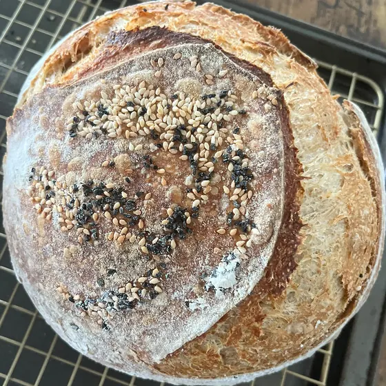 Une des miches de Suzie vue de haut : un pain rond au sésame et à la nigelle, ouvert le long d’une grande incision courbe.
