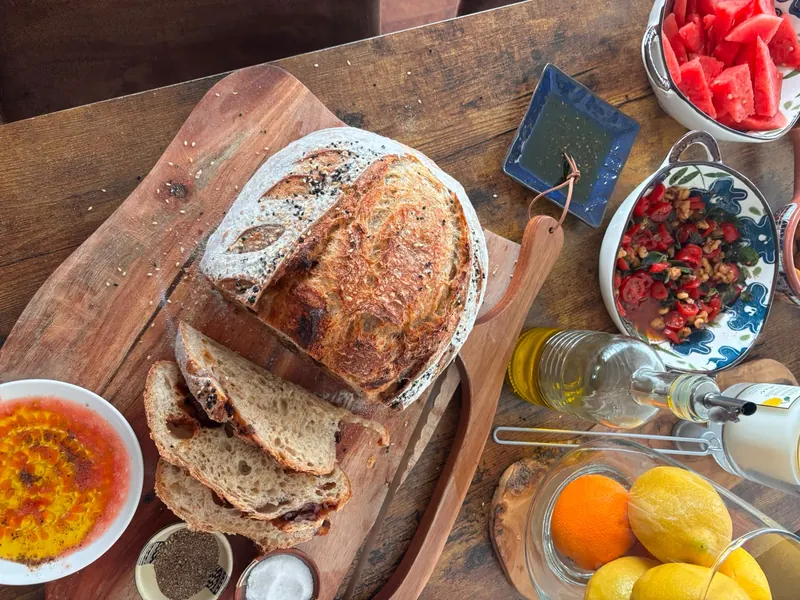 Sa miche tranchée, servie sur une planche avec de l’huile d’olive, des trempettes, du melon d’eau et des agrumes.