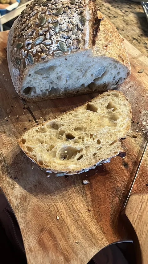 Une miche aux graines, tranchée, sur une planche de bois.